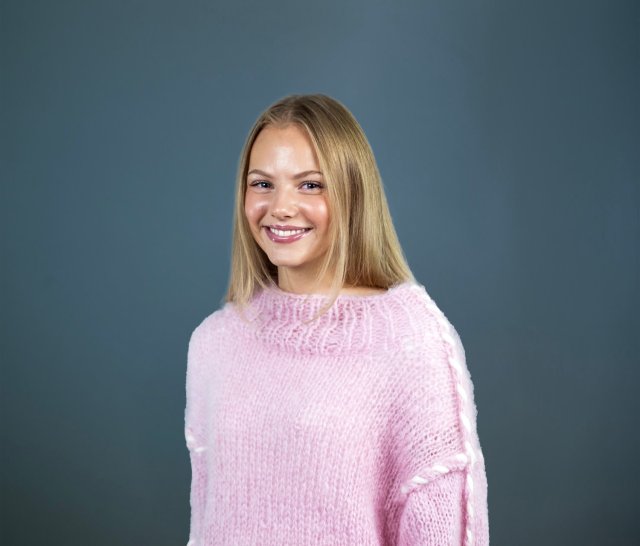 Jente med lyst, langt hår se i kamera og smiler