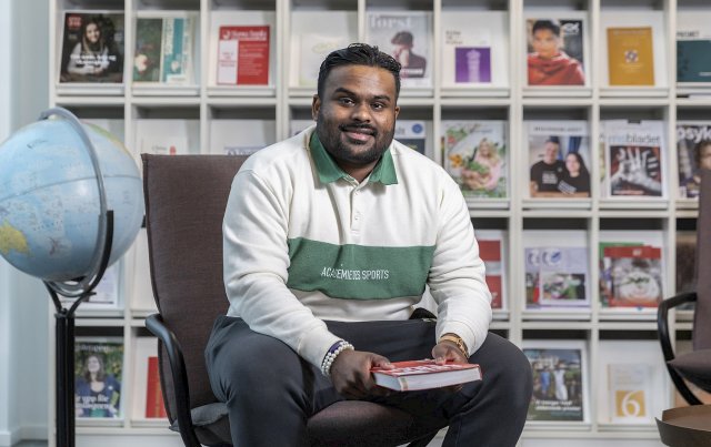 Ung mann sitter i en stol på et bibliotek.