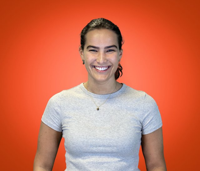 Jente med mørkt hår i hestehale smiler bredt mens hun ser rett i kamera