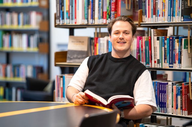 Portrett av Henrik foran en bokhylle på et biliotek