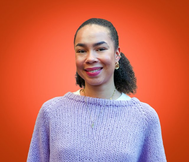 Jente med mørkt hår i hestehale smiler bredt mens hun ser rett i kamera