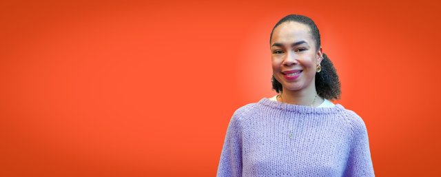 Jente med mørkt hår i hestehale smiler bredt mens hun ser rett i kamera