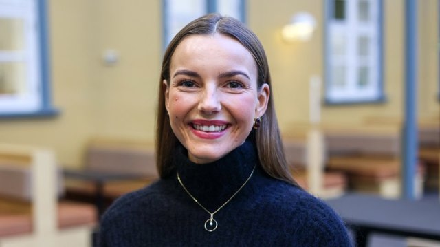 Jente med mørkt hår i hestehale smiler bredt mens hun ser rett i kamera