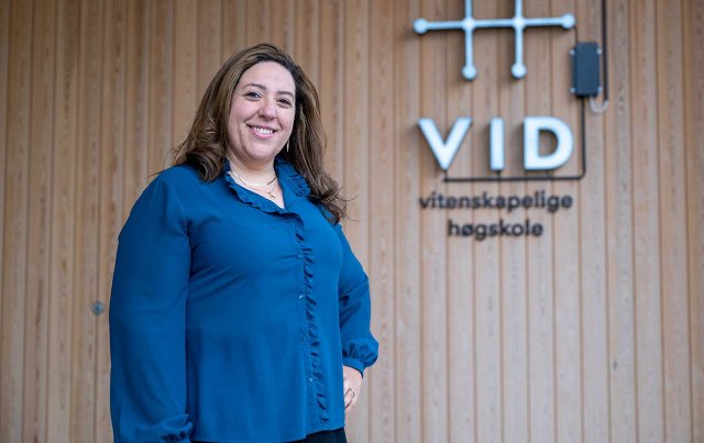 Dame i blå skjorte står foran en vegg med VID-logo