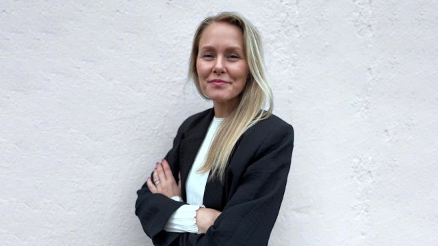 Dame i dressjakke poserer foran en hvit vegg