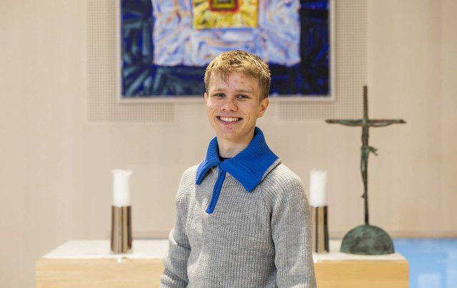 Ung gutt med strikkegenser står foran en altertavle.