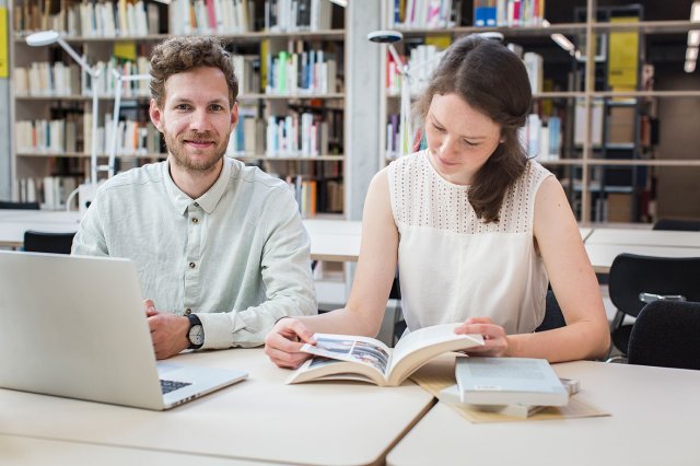 En gutt og en jente sitter på et bibliotek og studerer.