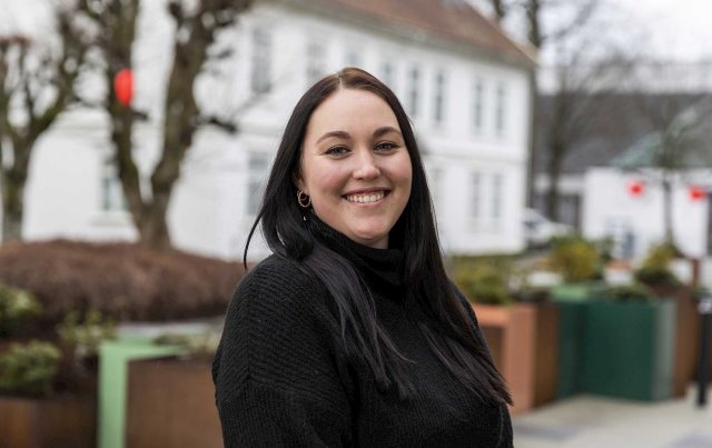 Smilende jente med mørkt langt hår se i kamera og smiler.